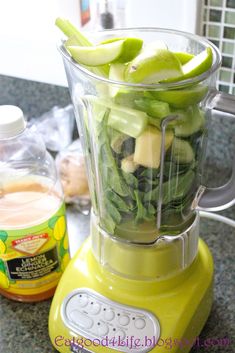 a yellow blender filled with green vegetables on top of a counter next to a jar of liquid