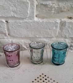 three glass cups sitting next to each other on a white counter top in front of a brick wall