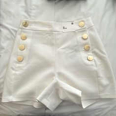 Elevate Your Wardrobe With These Stunning High-Rise Shorts That Exude Old Money Elegance. Crafted With A Premium Fabric Blend, These Shorts Feature A Flattering High-Waisted Silhouette And Eye-Catching Gold Button Detailing That Adds A Touch Of Sophistication. Designed To Flatter Your Figure, The High-Rise Waist Cinches At The Smallest Part Of Your Midsection, Creating A Sleek And Streamlined Look. The Fabric Is Soft, Breathable, And Slightly Stretchy For All-Day Comfort. Perfect For Dressy Casu Elegant High-waisted Shorts With Button Closure, Elegant High Waist Shorts With Button Closure, Elegant Shorts With Buttons, Elegant Short Bottoms With Button Closure, Elegant Short Bottoms With Buttons, Elegant Buttoned Shorts For Spring, White High-waist Bottoms With Button Closure, White High Waist Bottoms With Button Closure, High Waist White Bottoms With Button Closure