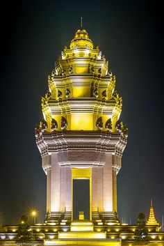 a tall tower that has a clock on it's side at night with lights in front of it