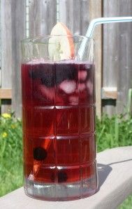 a glass filled with liquid sitting on top of a wooden table next to a fence