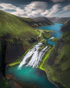 an aerial view of a waterfall in the middle of a green valley with blue water