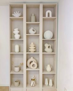 a white shelf with vases and other items on it's shelves in a room