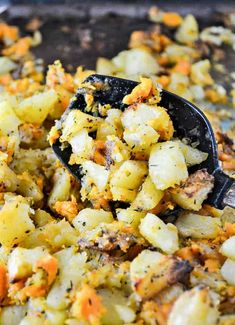 a spoon full of food sitting on top of a pan filled with potatoes and carrots