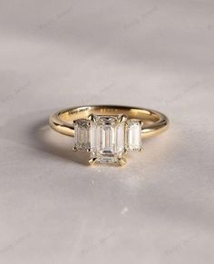 an emerald cut diamond ring with three baguets on the side, set in yellow gold