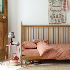 a bed with pink sheets and pillows in a room next to a wooden door,