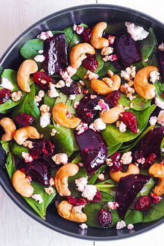 a salad with beets, walnuts and spinach in a black bowl on a white table