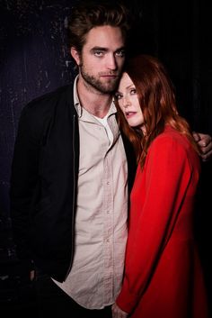 a man and woman standing next to each other in front of a black wall with paint splattered on it