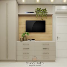 the television is mounted on the wall in the room with white cabinets and drawers, along with a potted plant