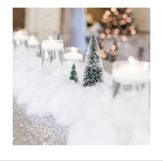 small christmas trees are sitting in the snow next to some candles and other holiday decorations