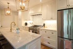 a white kitchen with marble counter tops and gold pendant lights hanging from the ceiling over the stove