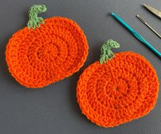 two crocheted pumpkins sitting on top of a table next to knitting needles