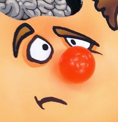 a close up of a clown's face with a red ball in his mouth