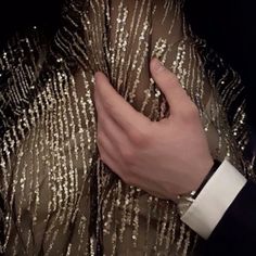 a close up of a person wearing a gold dress and holding their hand on his chest