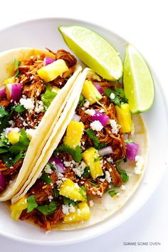 two tacos with shredded meat, pineapples and onions on a white plate