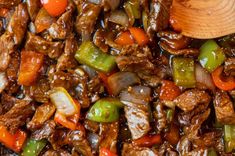 a wooden spoon in a skillet filled with beef and vegetables