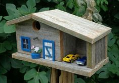 a wooden birdhouse with two cars parked in the window and one car on the porch