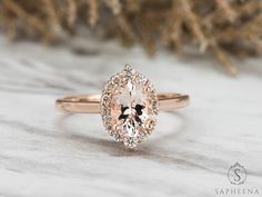 an oval shaped morganite and diamond ring on top of a white marble surface with some branches in the background