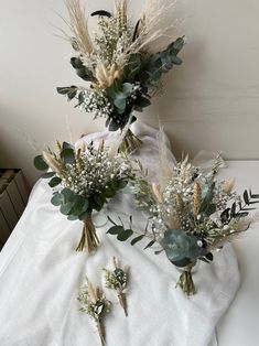 three bouquets of flowers are sitting on a white cloth with greenery and leaves