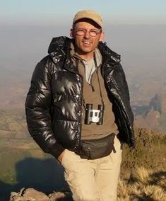 a man standing on top of a mountain with his hands in his pockets and looking at the camera