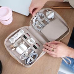 a woman is holding an open case with various cords and plugs in it on a table