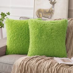 two green pillows sitting on top of a couch next to a plant in a vase