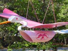 two pink and white kites hanging from strings in front of some trees with green leaves