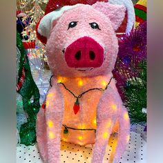 a pink stuffed pig wearing a santa hat and lights on it's chest sitting in front of christmas decorations