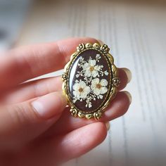 a person holding a ring with flowers on it in their left hand and an open book in the background