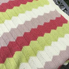 a crocheted blanket is sitting on a chair next to some grass and flowers