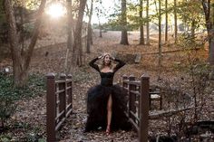 a woman in a black dress is sitting on a bridge with her hands behind her head