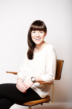 a woman sitting on top of a wooden chair with her legs crossed and smiling at the camera