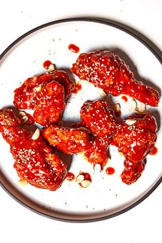 a white plate topped with chicken wings covered in marinara sauce and garlic flakes