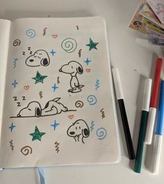 an open notebook with stickers and markers on the pages, next to some pens