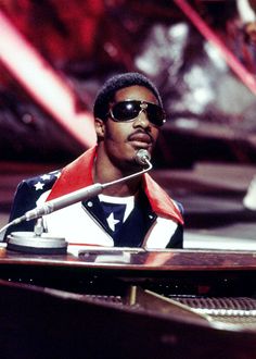 a man sitting at a piano in front of other people wearing red and white outfits