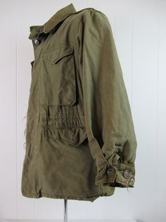 "Vintage 1940s WWII U.S. Army military M-1943 field jacket. Made of green cotton. Has chinstrap, button front, four pockets, shoulder epaulets and drawstring at the waist. Size 34R. Size small/medium. Actual measurements are: 42\" at the chest 40\" at the waist 18.5\" shoulder seam to shoulder seam 21\" shoulder seam to cuff 30\" overall length In wrecked condition. Has small spots of tar, paint, some cracked and replaced buttons. Wear hole at collar." Combat Style Khaki Cotton Utility Jacket, Khaki Cotton Combat Utility Jacket, Vintage Olive Utility Jacket For Fall, Vintage Khaki Parka For Fall, Vintage Khaki Utility Jacket For Winter, Vintage Khaki Utility Jacket With Flap Pockets, Vintage Khaki Utility Jacket With Buttons, Vintage Olive Outerwear With Buttons, Vintage Fall Parka With Flap Pockets