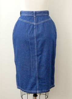 "~ 1970s denim skirt featuring, a high yoked waist lots of white top stitching belt loops on the waistband a pocket at each hip it snaps all the way down the front falls to just below the knee ~ of a mid weight, cotton denim in a dark blue ~ labeled \"Cheryl Tiegs\", (supermodel turned fashionista), this is tagged a size 8, measurements when laid out flat are: 12 1/4 inches at the waist 18 inches at the hip 25 inches from waist to hem ~ would best fit a size small to medium ~ in good, preworn, v