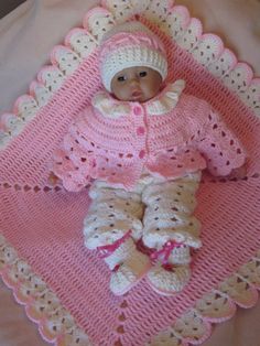 a baby doll laying on top of a crocheted blanket and wearing a pink outfit