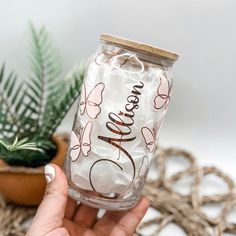 a hand holding a clear glass with the words happy birthday on it next to a potted plant