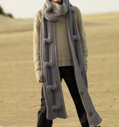 a woman standing on top of a sandy beach wearing a gray scarf and black pants