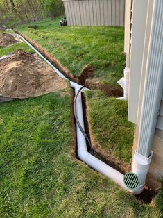 a drain in the ground next to a house with grass and dirt on the ground