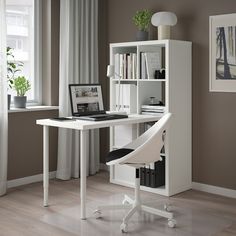 a computer desk with a laptop on top of it next to a book shelf and window