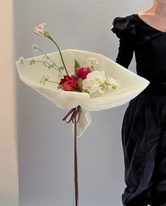 a woman holding a bouquet of flowers in front of a white wall and wearing a black dress