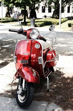 a red scooter parked on the side of a road next to a tree