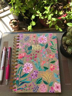 a notebook sitting on top of a table next to a potted plant and pen