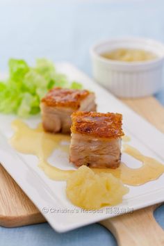 two pieces of meat sitting on top of a white plate next to potatoes and lettuce