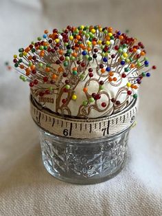 there is a glass jar that has beads on it and a tape measure in front of it