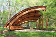 a wooden structure in the middle of a forest with benches under it and trees around