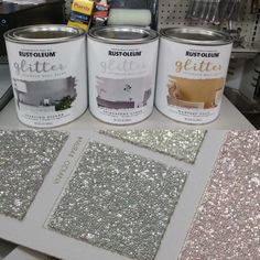 three cans of paint sitting on top of a table next to some glittery papers