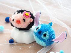 two small stuffed animals sitting on top of a white object with blue and pink pom poms